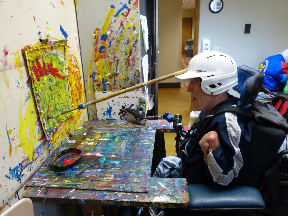 man in wheelchair painting with adaptive equipment